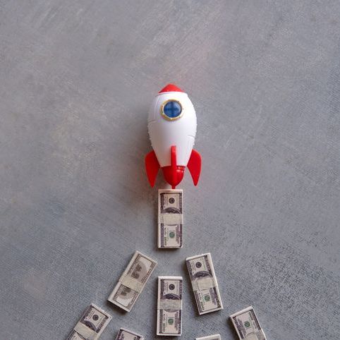 toy rocket shooting up and trailed by dollar bills
